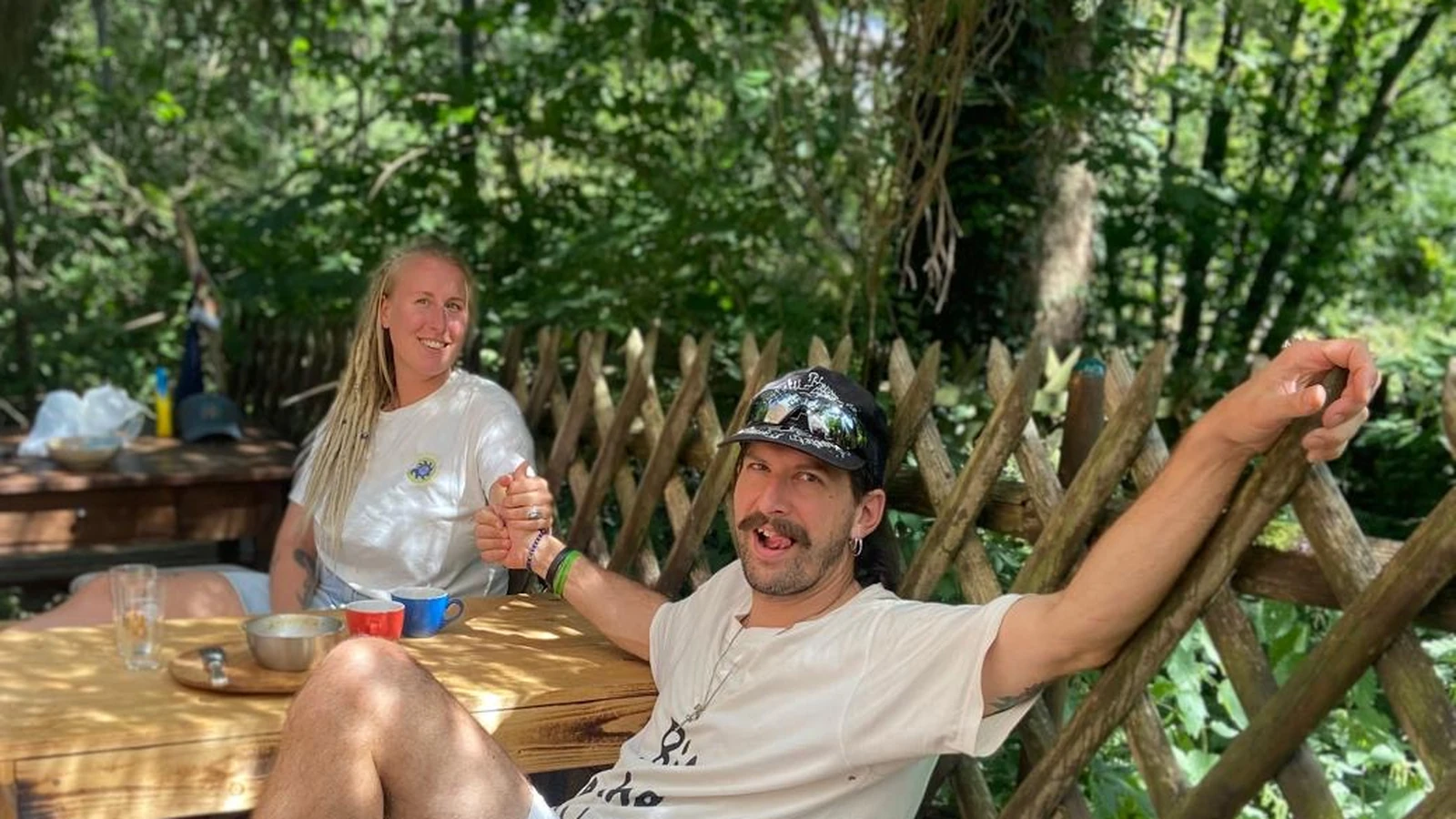 Sebastian und Sonja von SSM267 sitzen gemeinsam draußen am Holztisch und halten sich an den Händen.